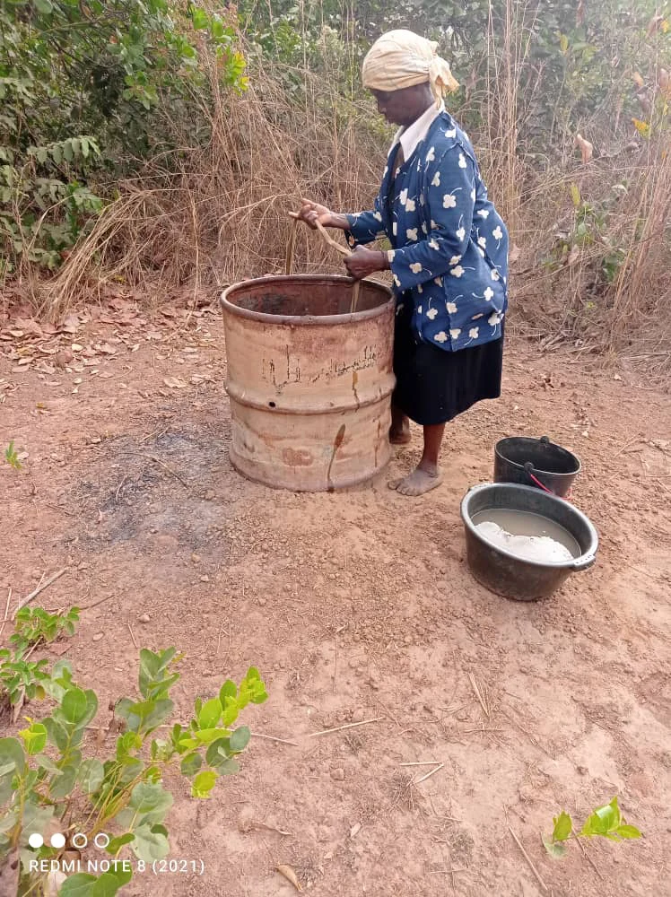 Mujer sacando agua junto a un bidón y barreños en un punto de agua rural