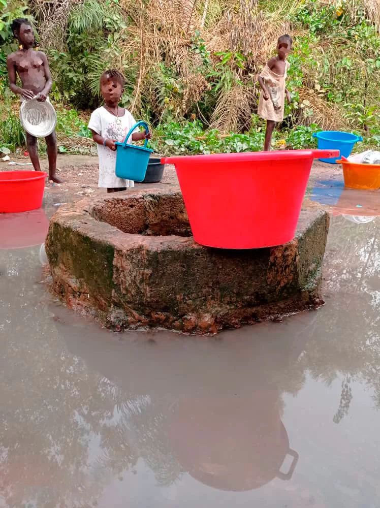 Punto de agua con barreño rojo y una niña recogiendo agua