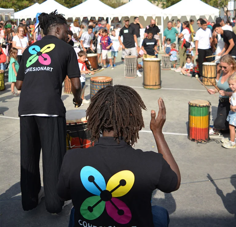 Percusionistas con camiseta de CohesionART tocando djembés ante el público