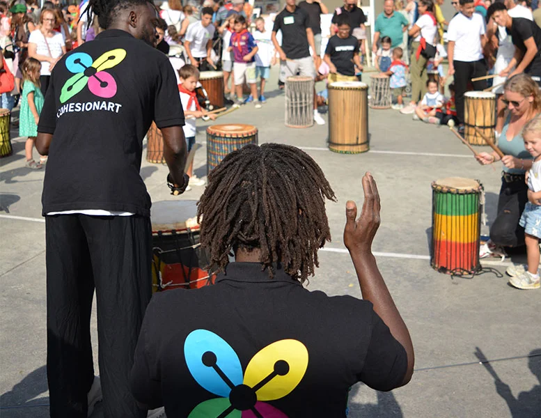 Percusionistas con camiseta de CohesionART tocando djembés ante el público